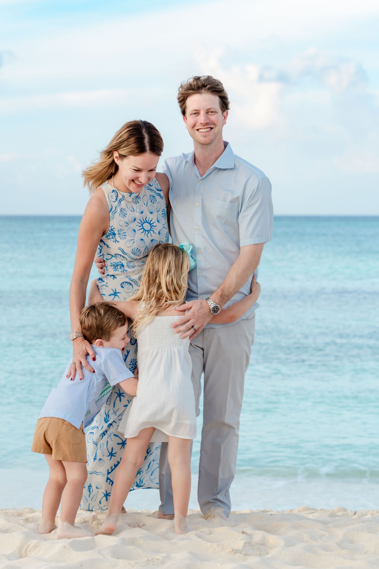 A family shares joyful moments together on a pristine beach with turquoise waters and white sand in the background.