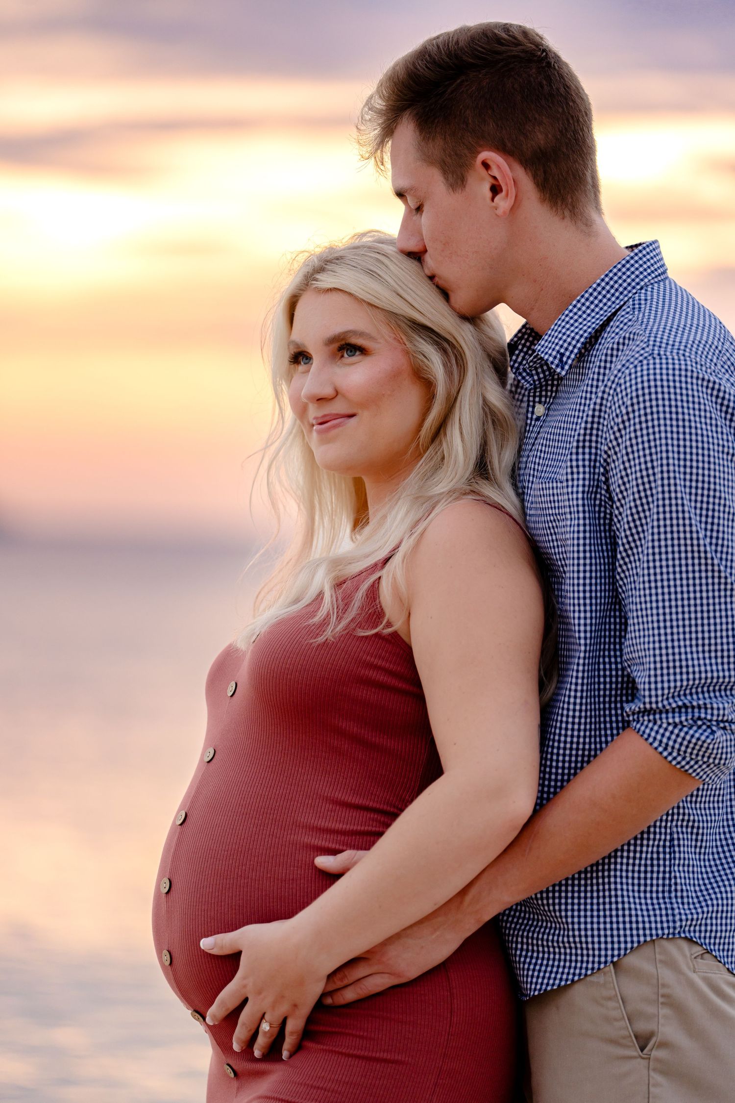 Couple embraces during sunset maternity photo session on beach.