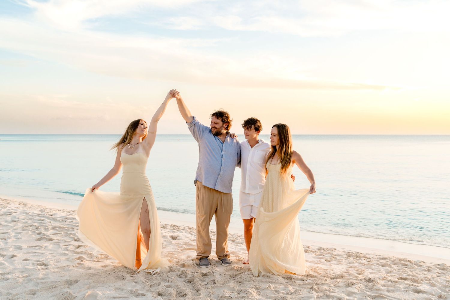 A group poses together on a beach at sunset with flowing dresses creating movement.