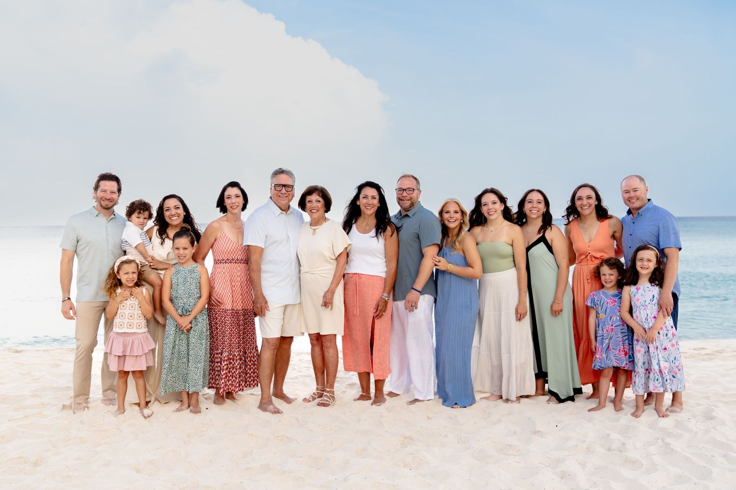 Large family group in coordinated outfits poses together on a white sandy beach.