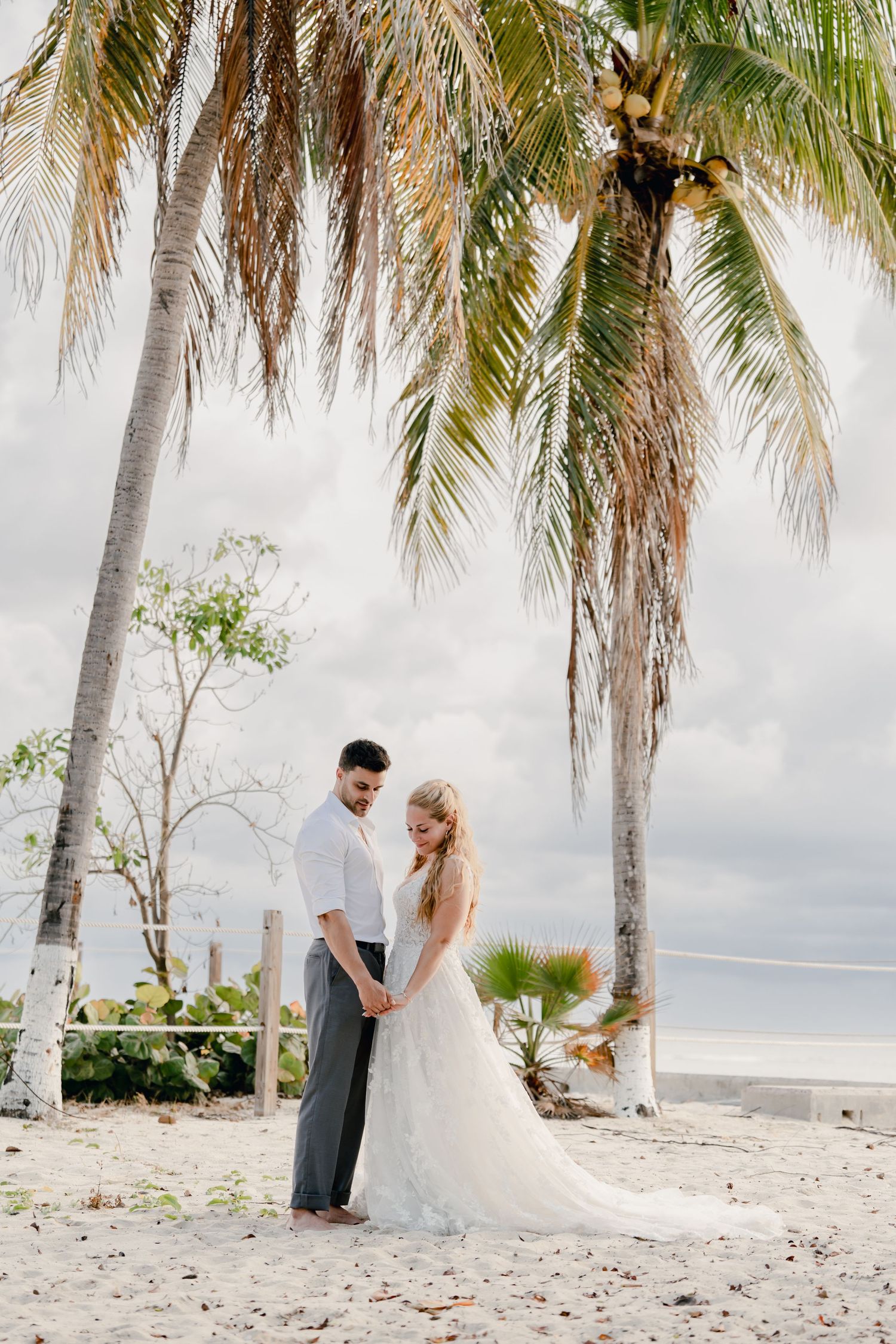 Beach wedding portrait under palm trees with cloudy sky backdrop.