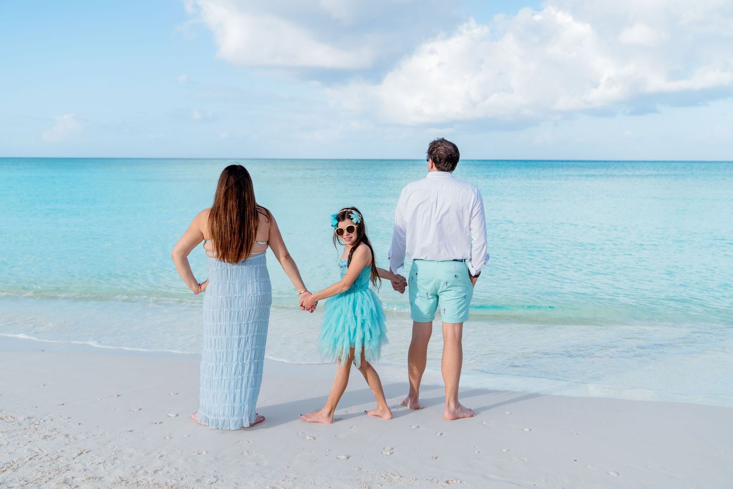 Couple in coordinating blue outfits walking along a pristine tropical beach with turquoise ocean waters.