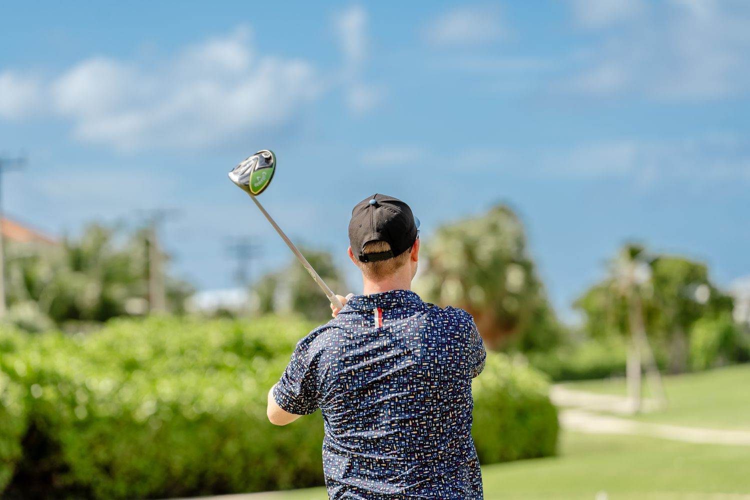 Golfer taking a swing on a lush green course under blue skies.
