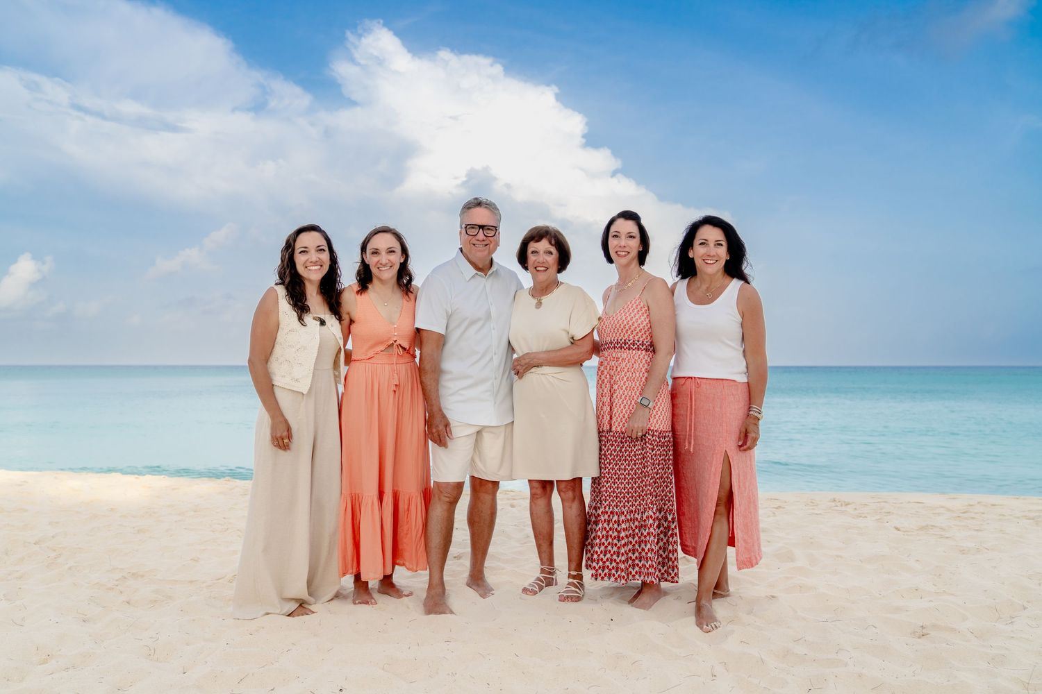 Group portrait on a tropical beach wearing coral and neutral colored dresses.