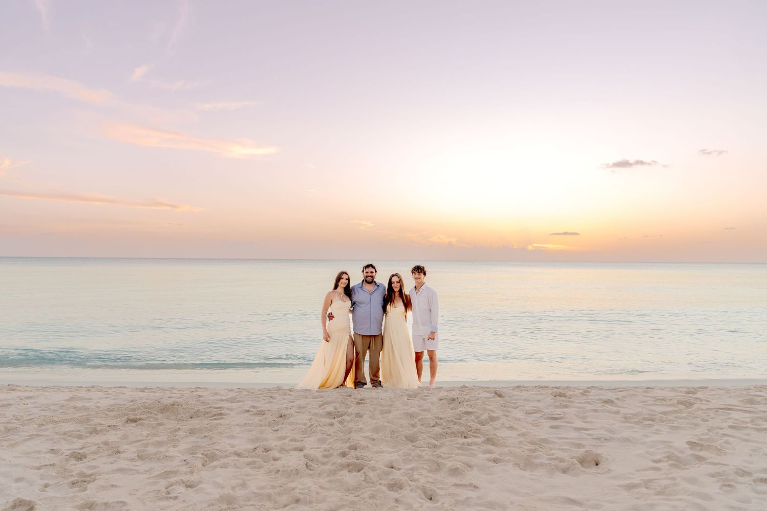 Silhouettes of people walking on a beach against a pastel sunset sky.