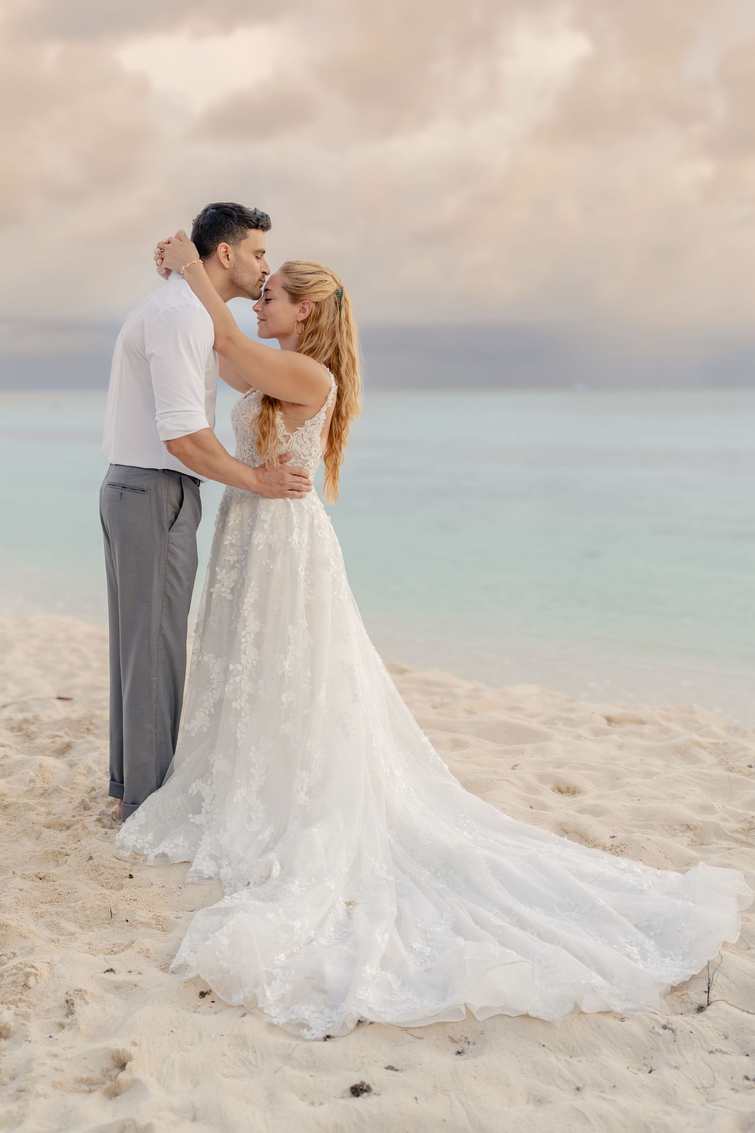 A couple shares an intimate dance moment on a tropical beach with turquoise waters in the background.