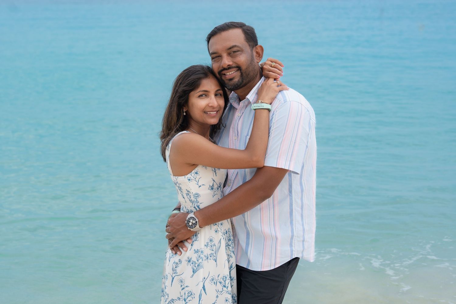 Couple embracing and smiling on a tropical beach with turquoise ocean water in the background.