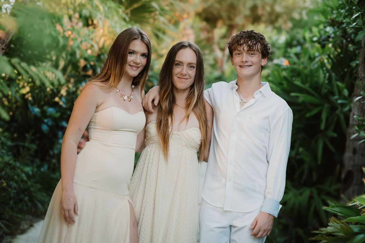 People dressed in white and beige gather for a photo in a tropical garden setting.