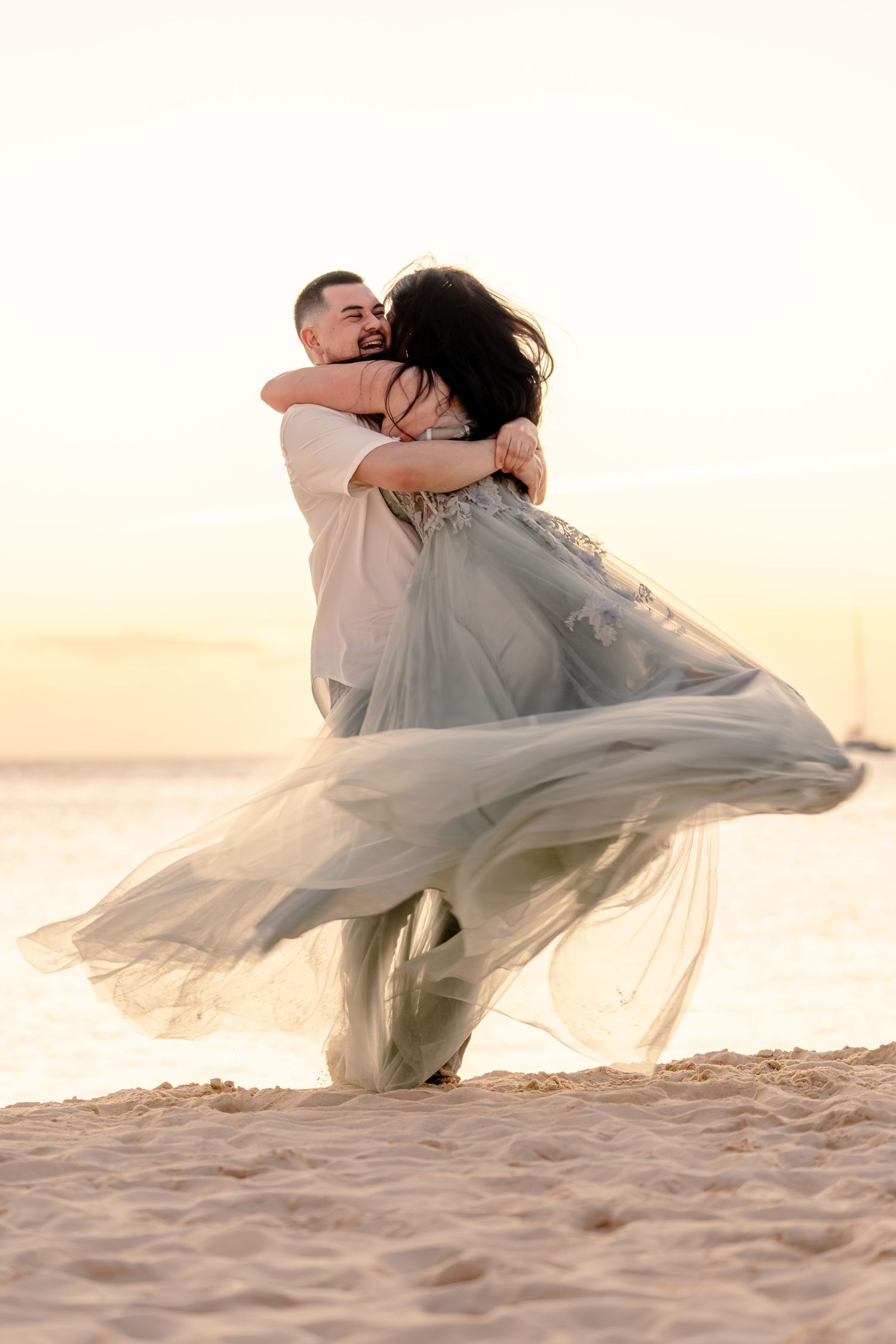Flowing blue-grey dress twirls dramatically during a romantic beach photoshoot at sunset.