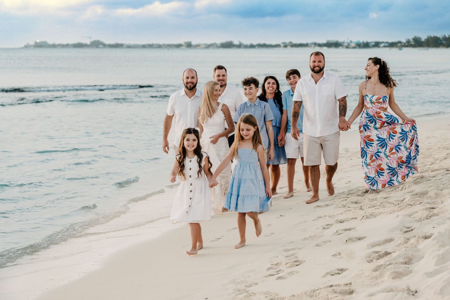 A group in coordinated blue and white outfits walks along a scenic beach at sunset.