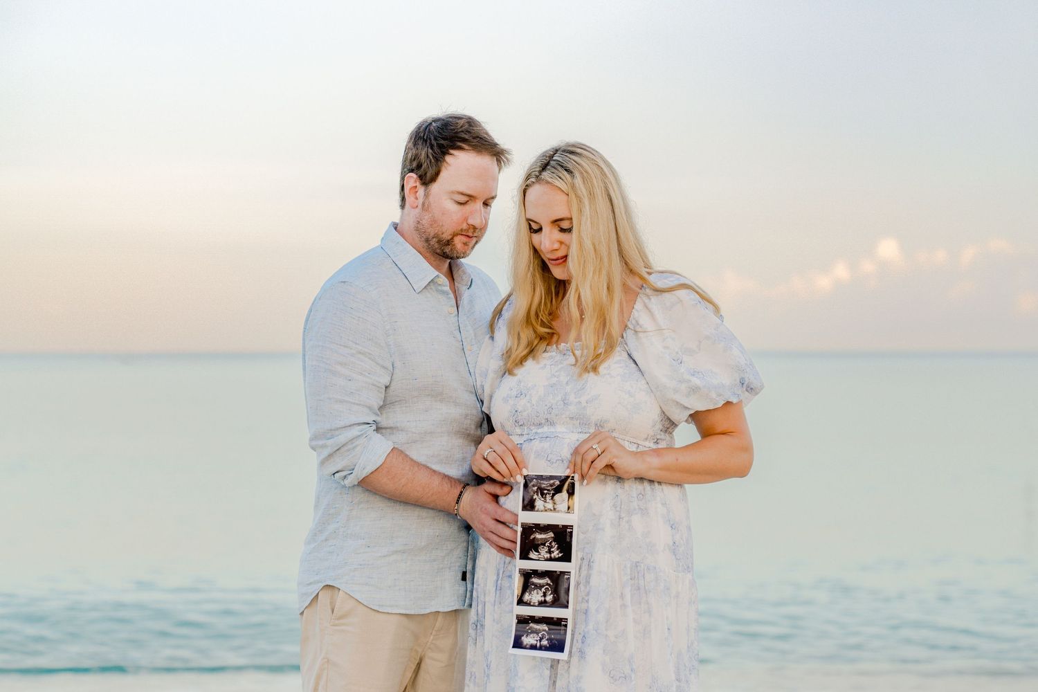 Romantic beach pregnancy announcement with couple sharing ultrasound photos at golden hour.