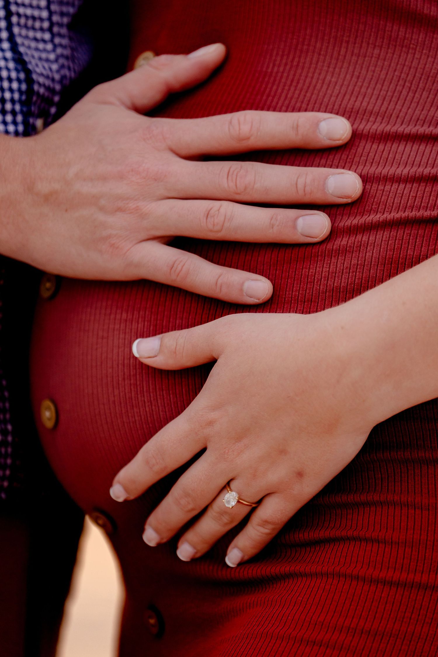 Close-up of hands resting on red fabric with engagement ring visible.