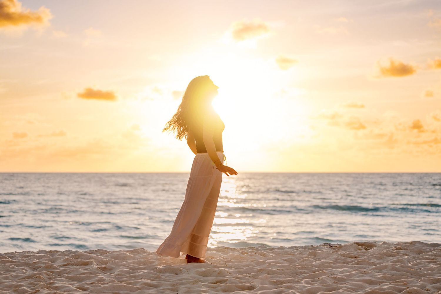 A silhouetted figure stands on a beach at sunset with golden clouds and ocean horizon.