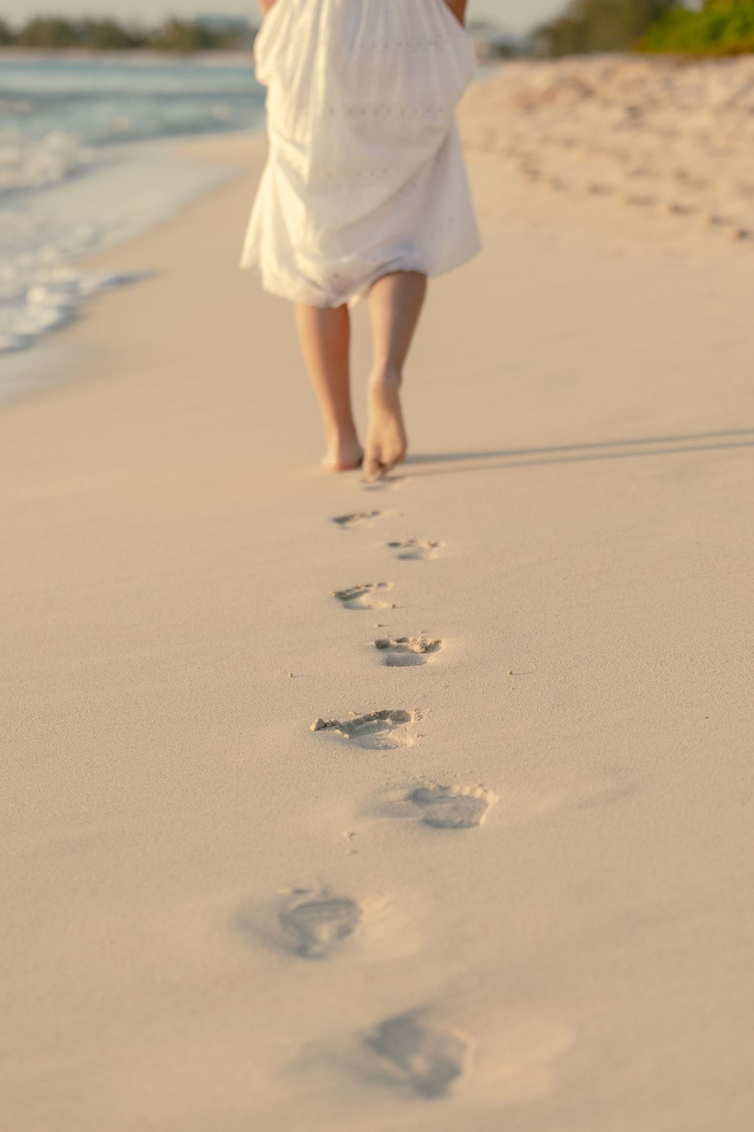 Footprints in pristine white sand along a peaceful beach at sunset.