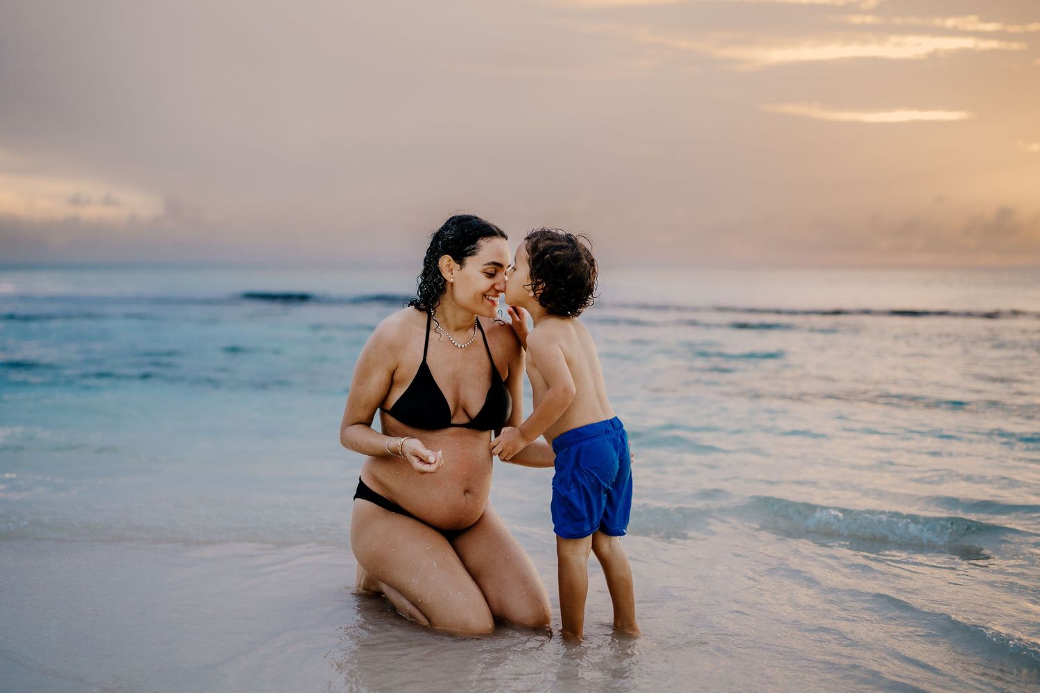 Expecting parents sharing intimate moment on beach during golden hour.