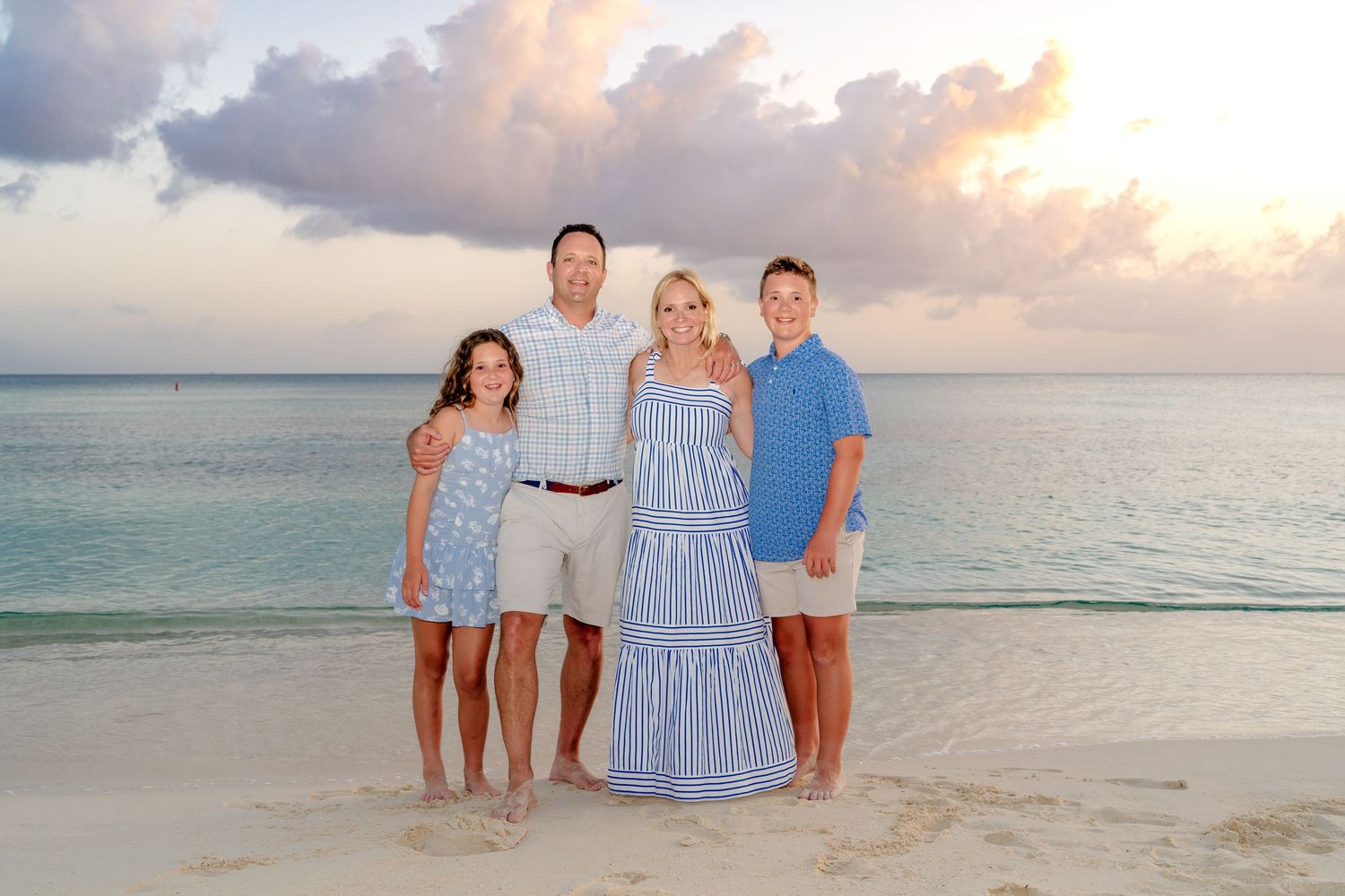 Small group in coordinated blue and white outfits poses on beach at sunset.