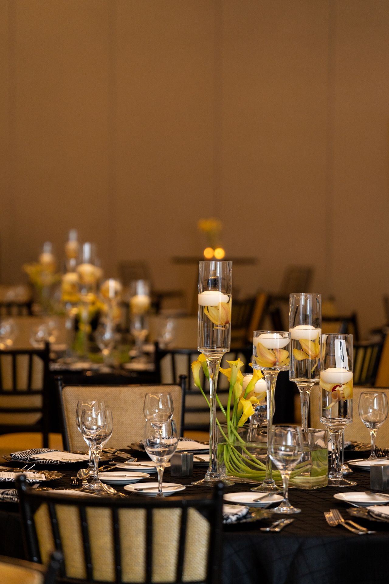 Formal table setting with floating candles and floral centerpieces on black tablecloth.