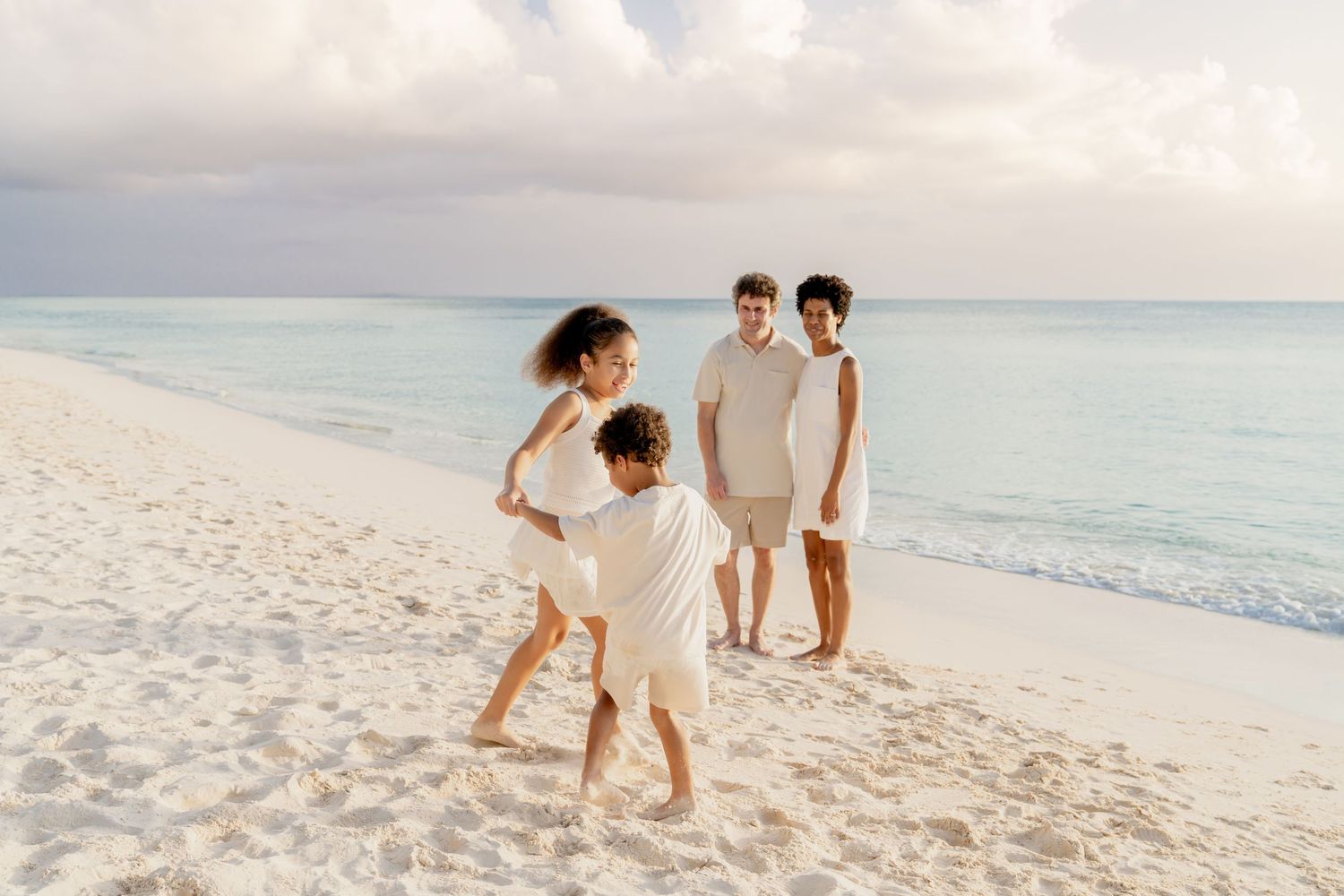 A group walks along a pristine white sand beach at sunset with ocean waves in the background.