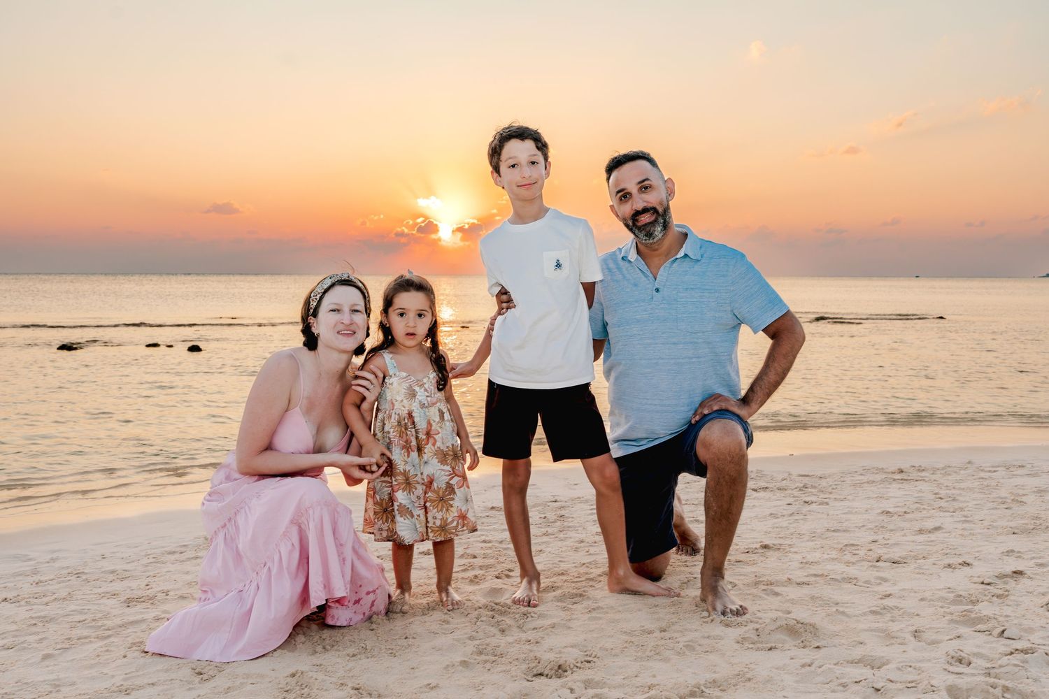 Family beach portraits captured during golden hour with the sun setting over the ocean.