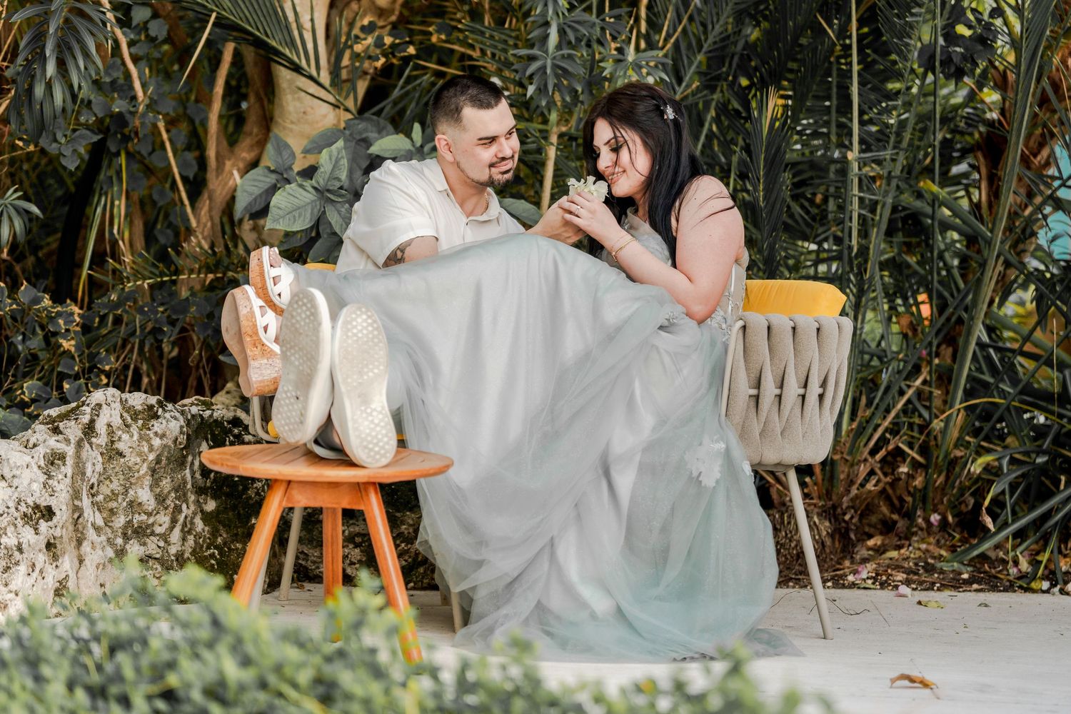 Couple posing for romantic photos in a garden with wooden furniture.