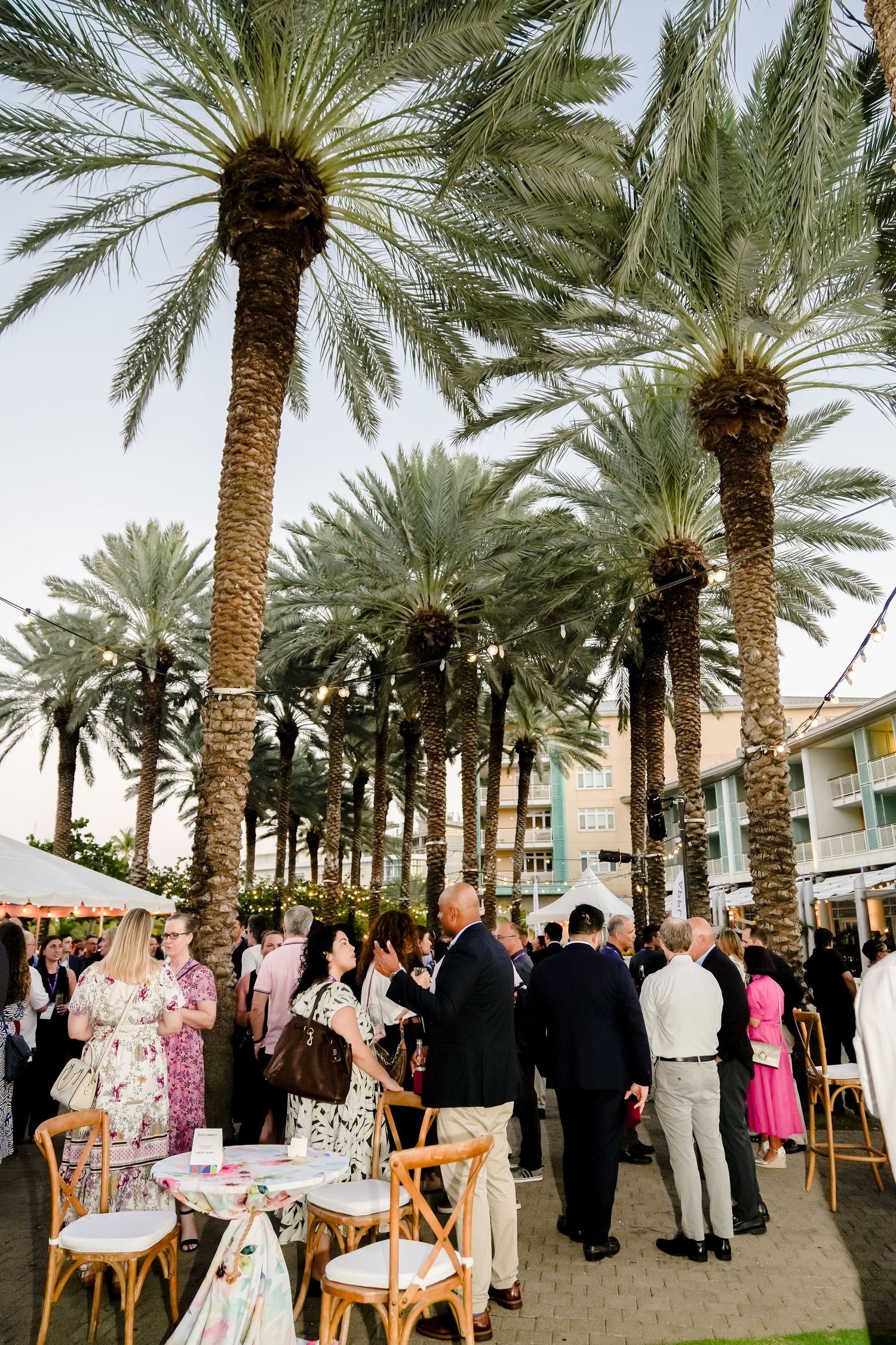 Elegant outdoor reception with palm trees and guests mingling under tropical landscaping.