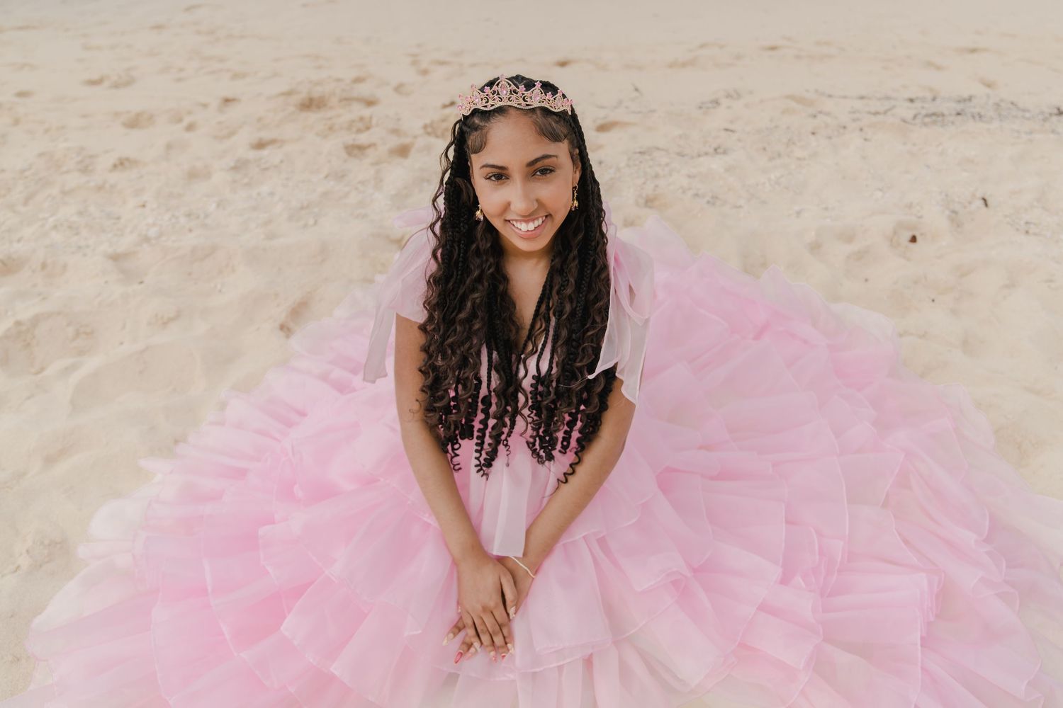 Person in elegant pink gown poses gracefully on tropical beach.
