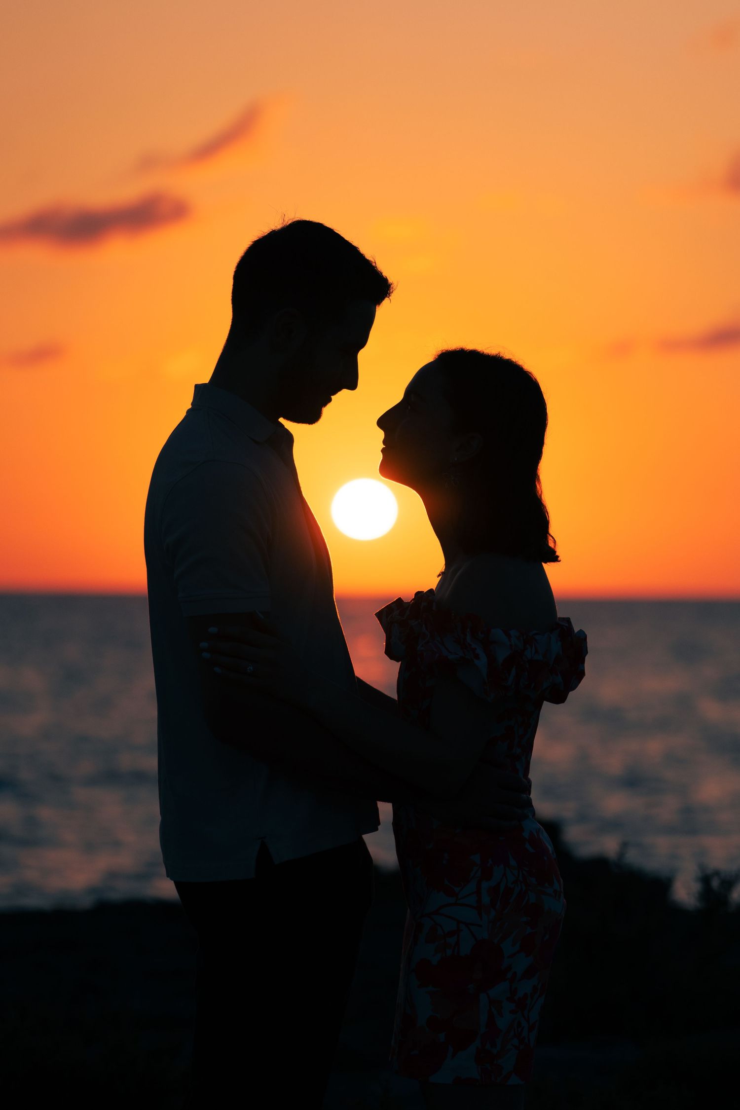 A silhouetted couple in a romantic pose against a vibrant orange sunset over the ocean.