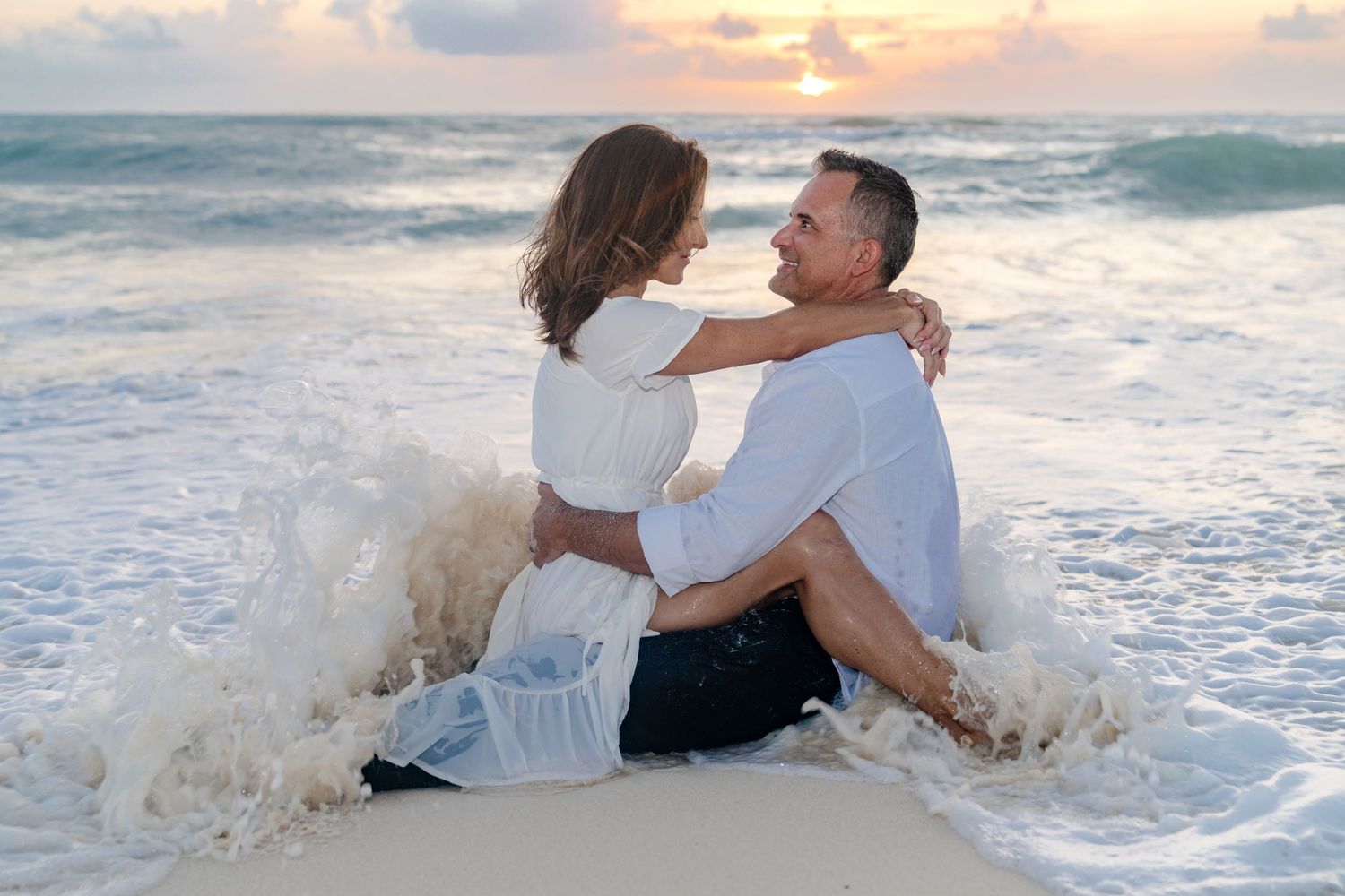 Couple playing in ocean waves during sunset beach photoshoot.