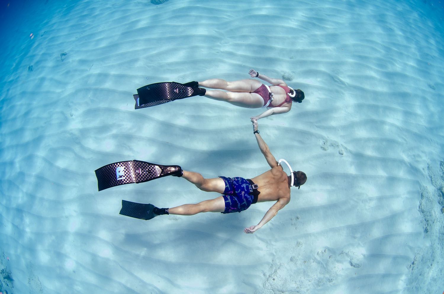 Two snorkelers floating in shallow clear waters viewed from above.