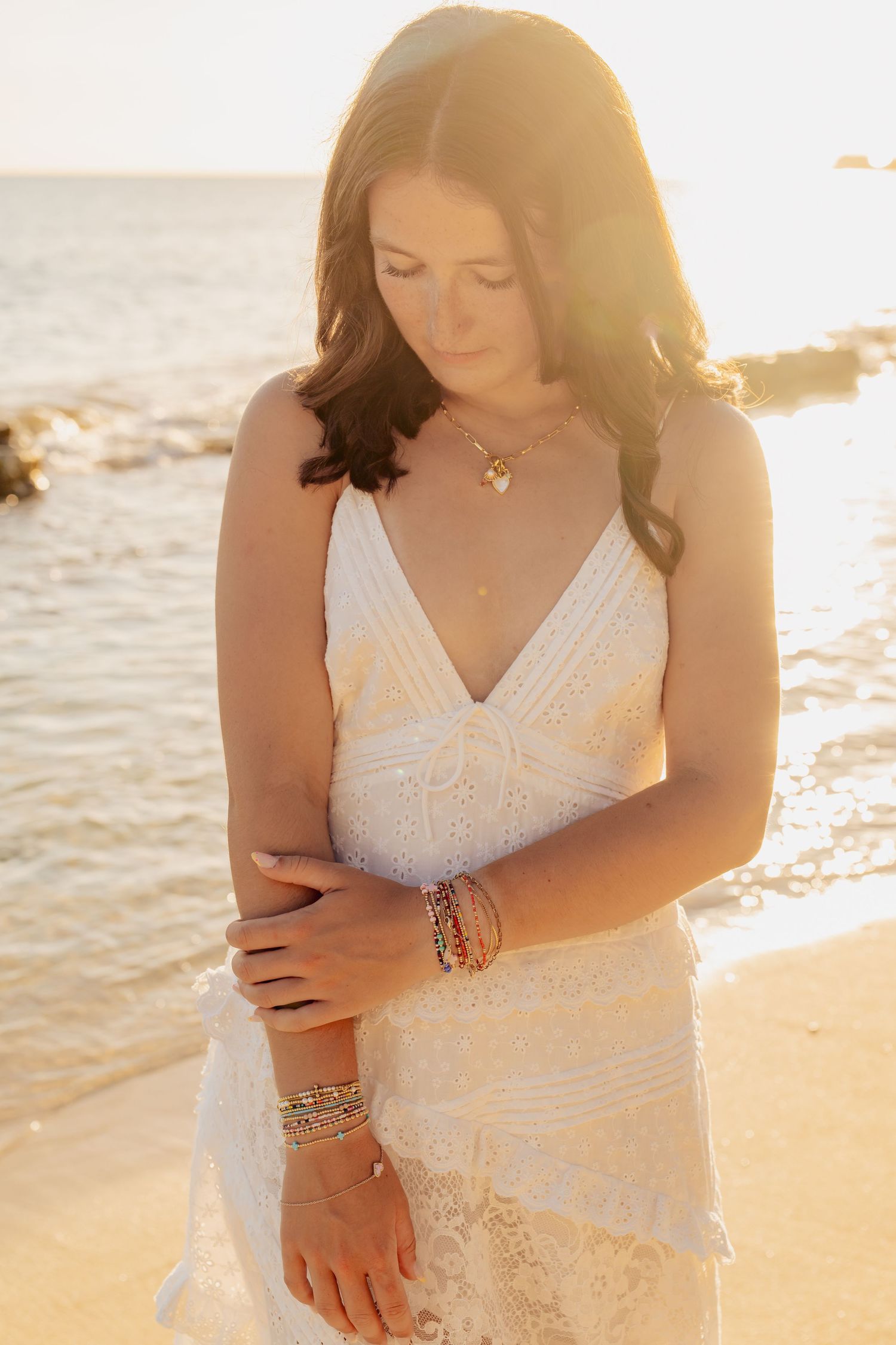 Close-up details of white lace dress and jewelry at sunset beach photoshoot.
