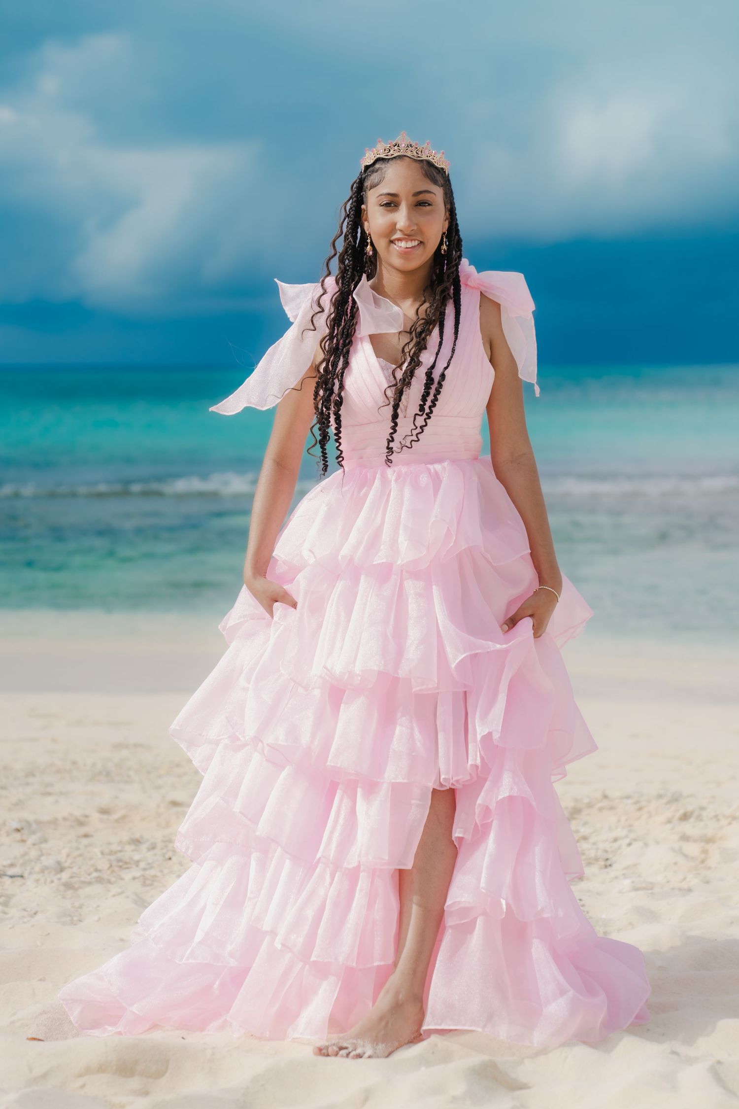 Figure in flowing pink tiered dress twirls on sandy beach.