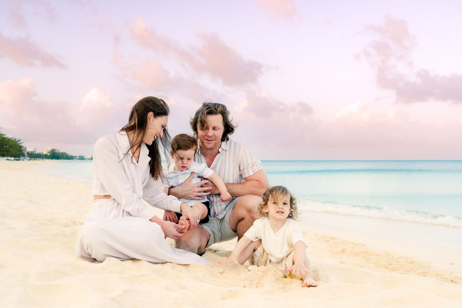Intimate family gathering on a tropical beach during sunset with soft pastel colors.