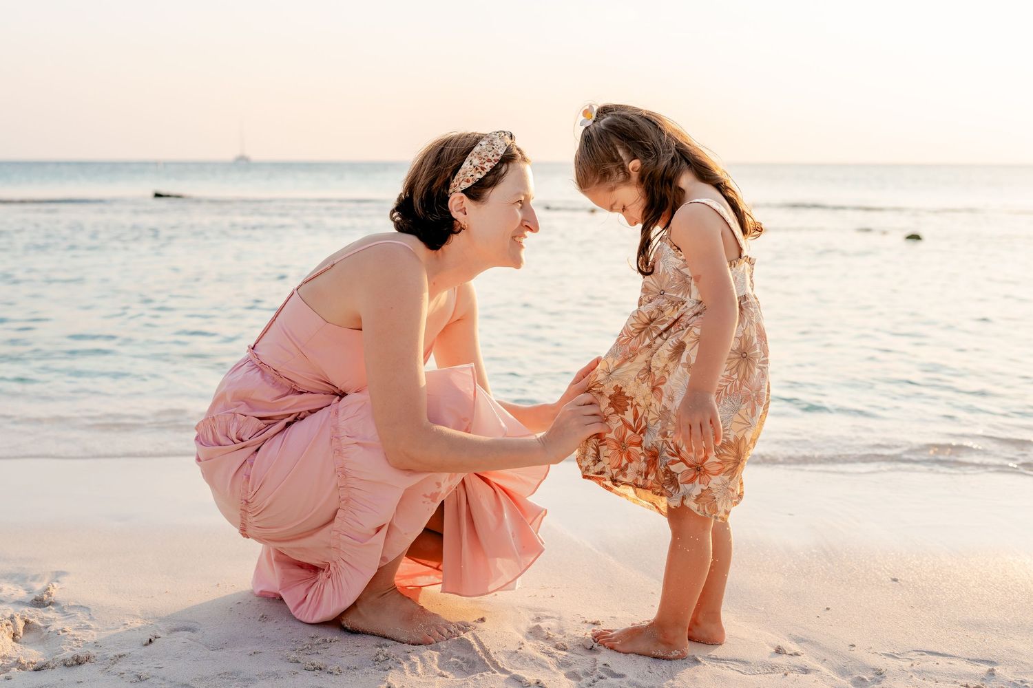 Intimate beach photoshoot with people in pink dresses playing in the sand at dusk.