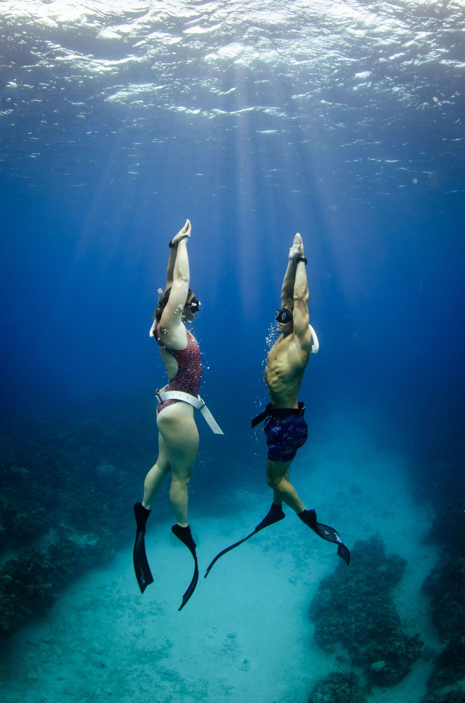 Two snorkelers diving vertically in deep blue ocean waters with sunbeams streaming down.