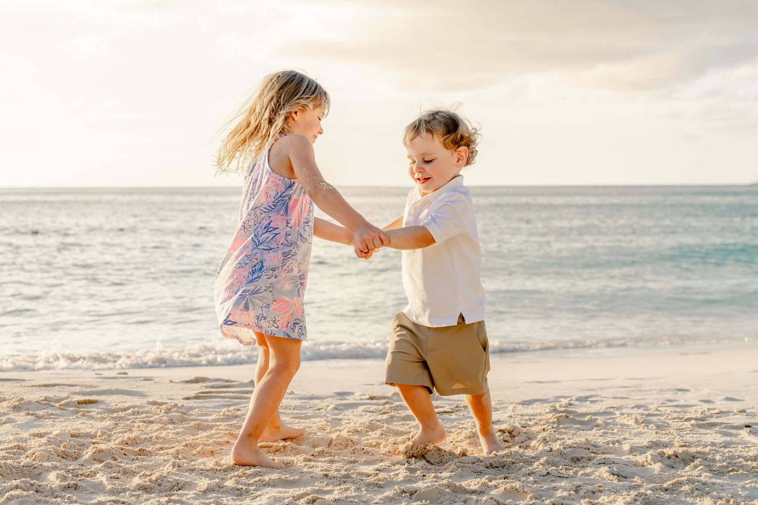 A family plays together on a sunny beach at sunset, running and splashing in the golden light.