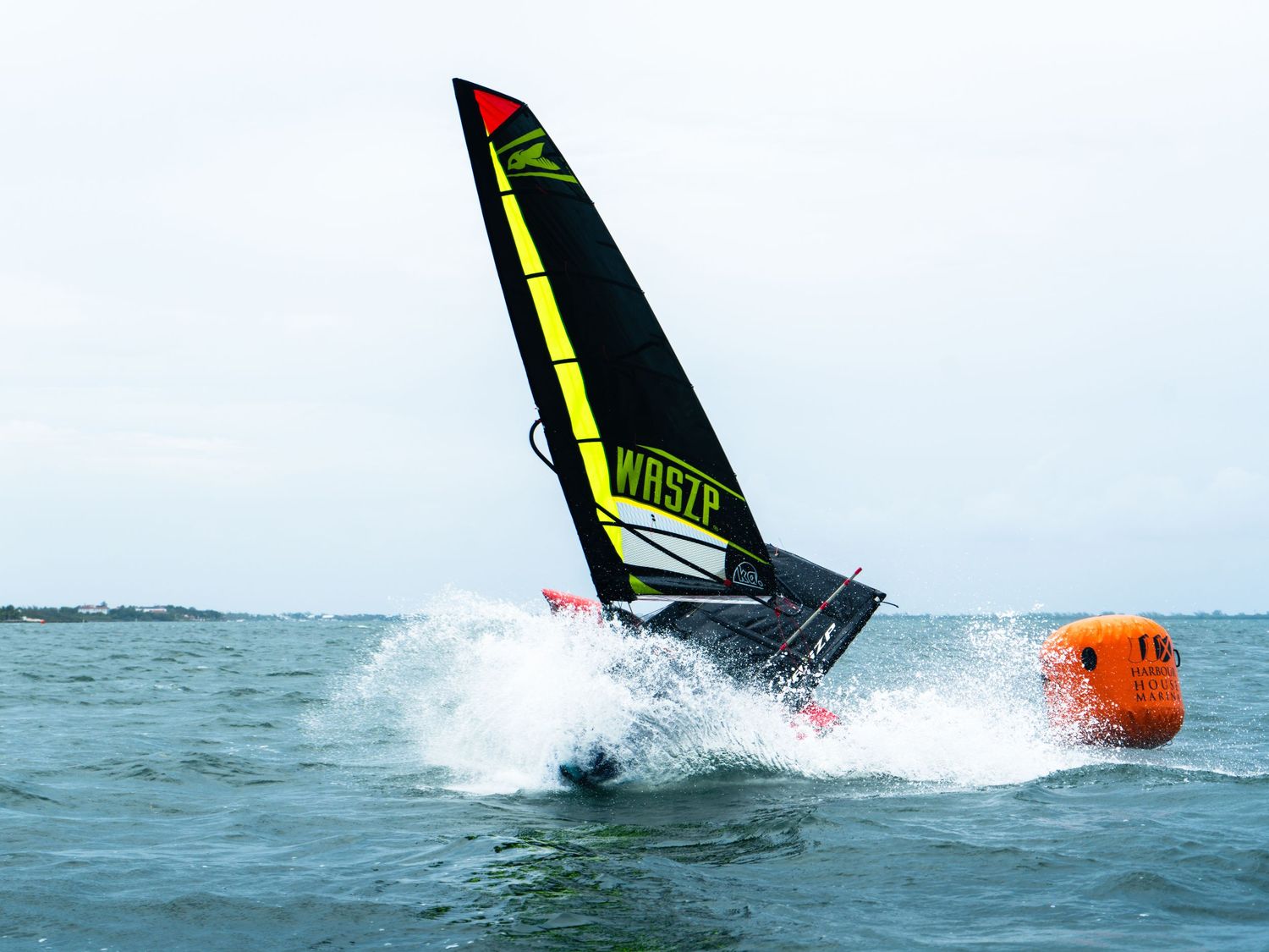 Windsurfer performing an aggressive turn near a race buoy with splashing waves.