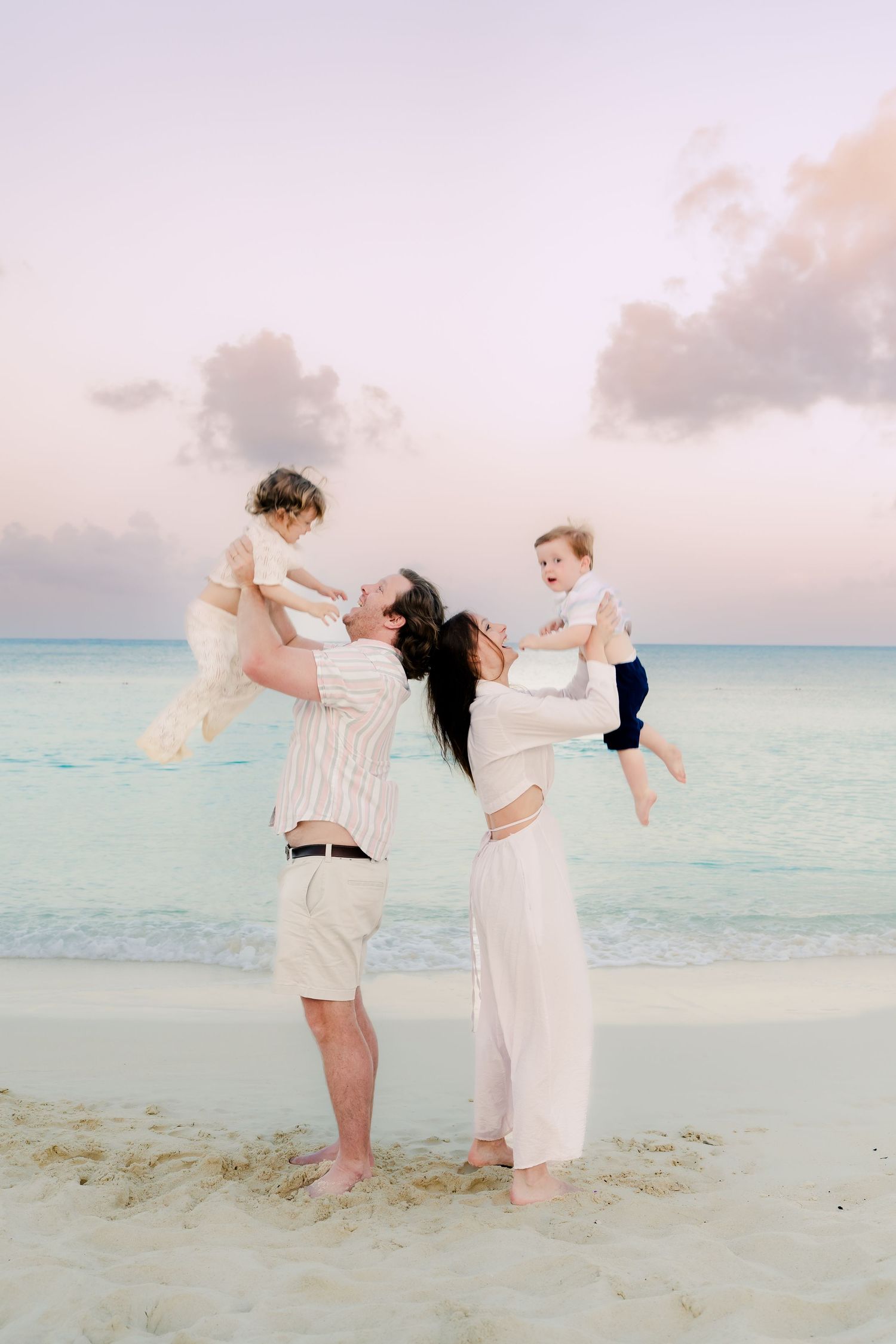 Playful family moment captured on a white sandy beach with crystal clear ocean waters at dusk.