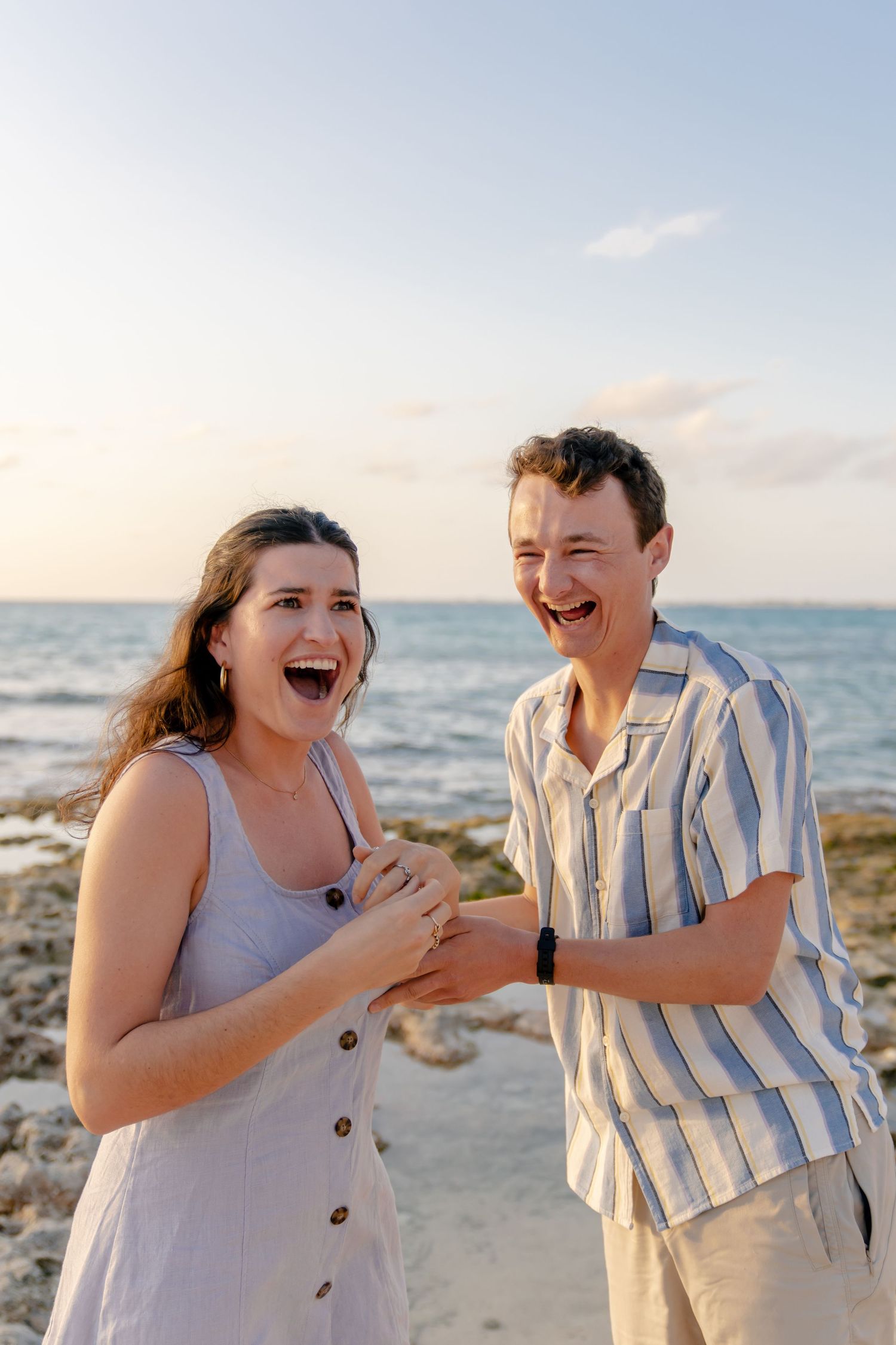 Couple laughing together on beach during casual sunset photoshoot.