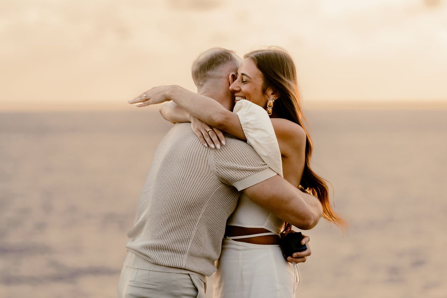 A passionate embrace between a couple during their beach engagement session at sunset.