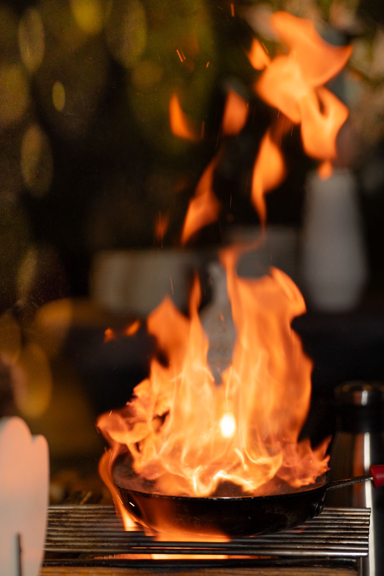 Bright orange flames dance across a grill grate during nighttime cooking.