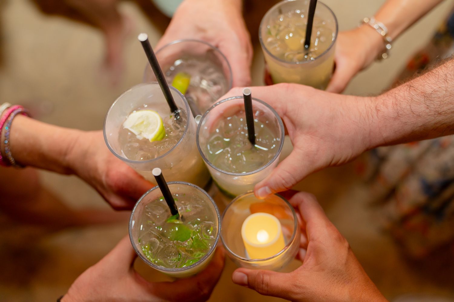 Multiple hands toasting with cocktail glasses in a celebratory moment.