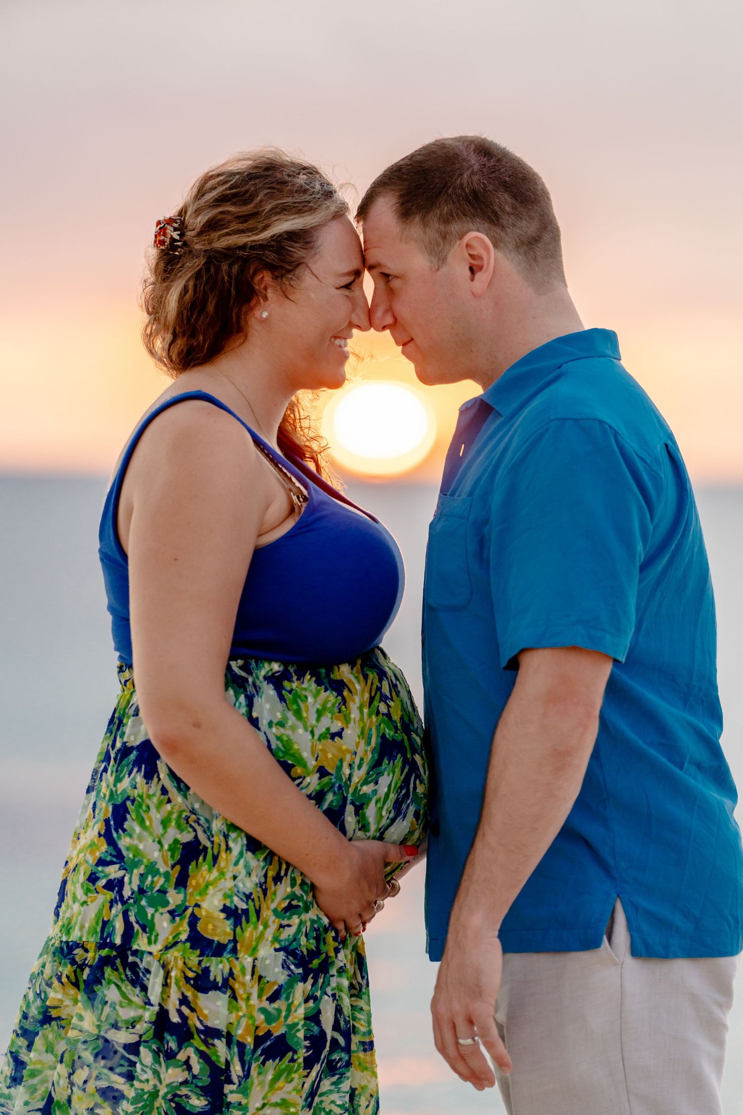 Intimate couple portraits on beach with sunset backdrop and flowing floral dress.