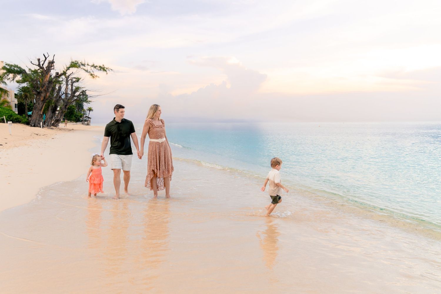 Family walking along a pristine beach at sunset with turquoise waters and soft sand.