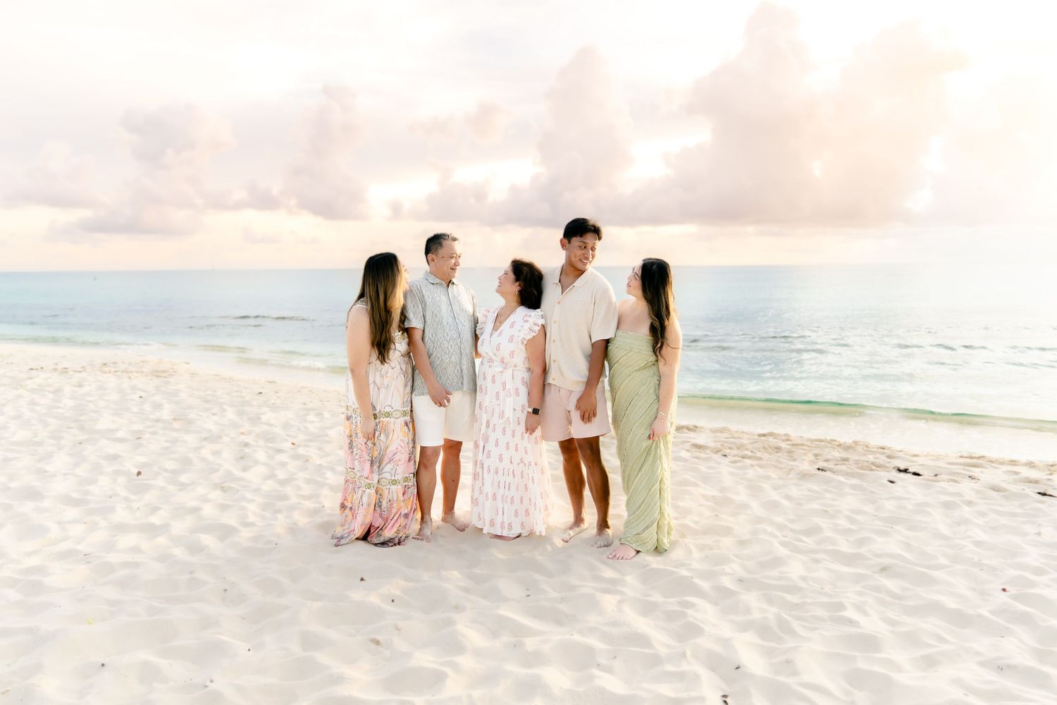 Family group standing together on white sand beach during golden hour.