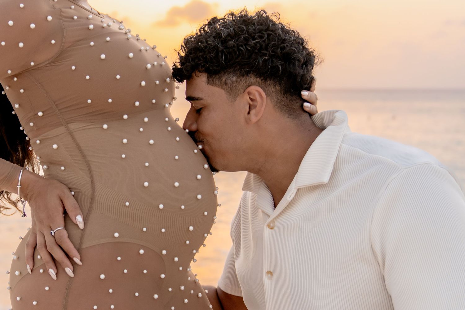 Close-up maternity photo showing tender moment on beach at sunset.