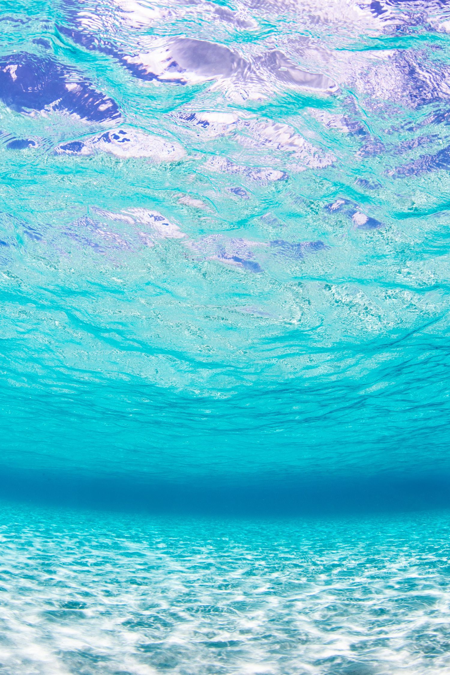 Crystal clear turquoise waters seen from beneath the surface with sunlight streaming through rippling waves.