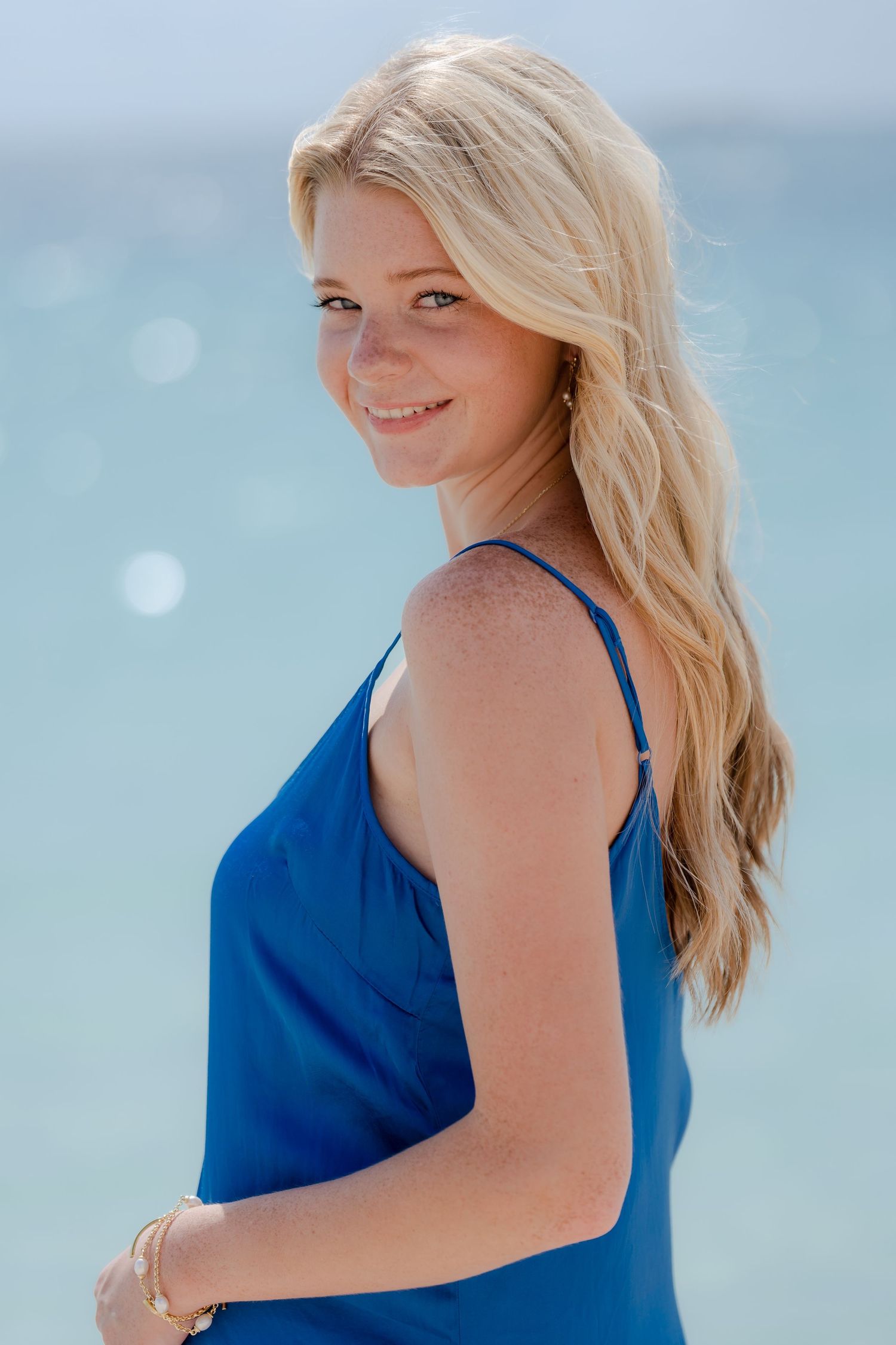 Woman in bright blue top poses outdoors with ocean view and natural lighting.