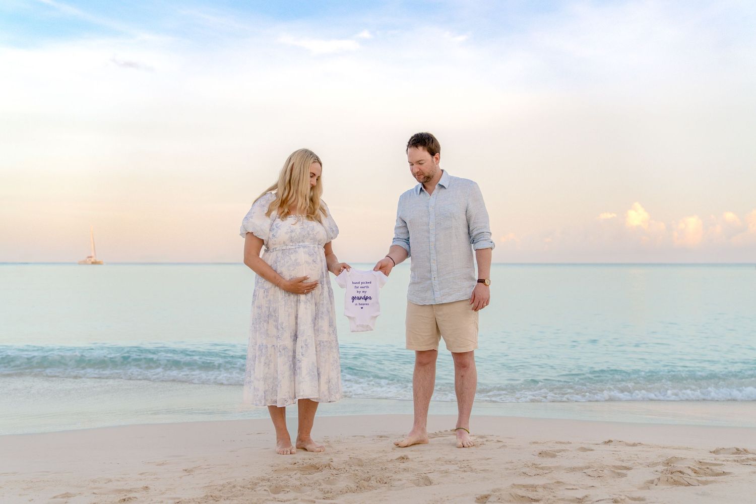 Expectant couple walking along shoreline while holding ultrasound photos during beach photoshoot.