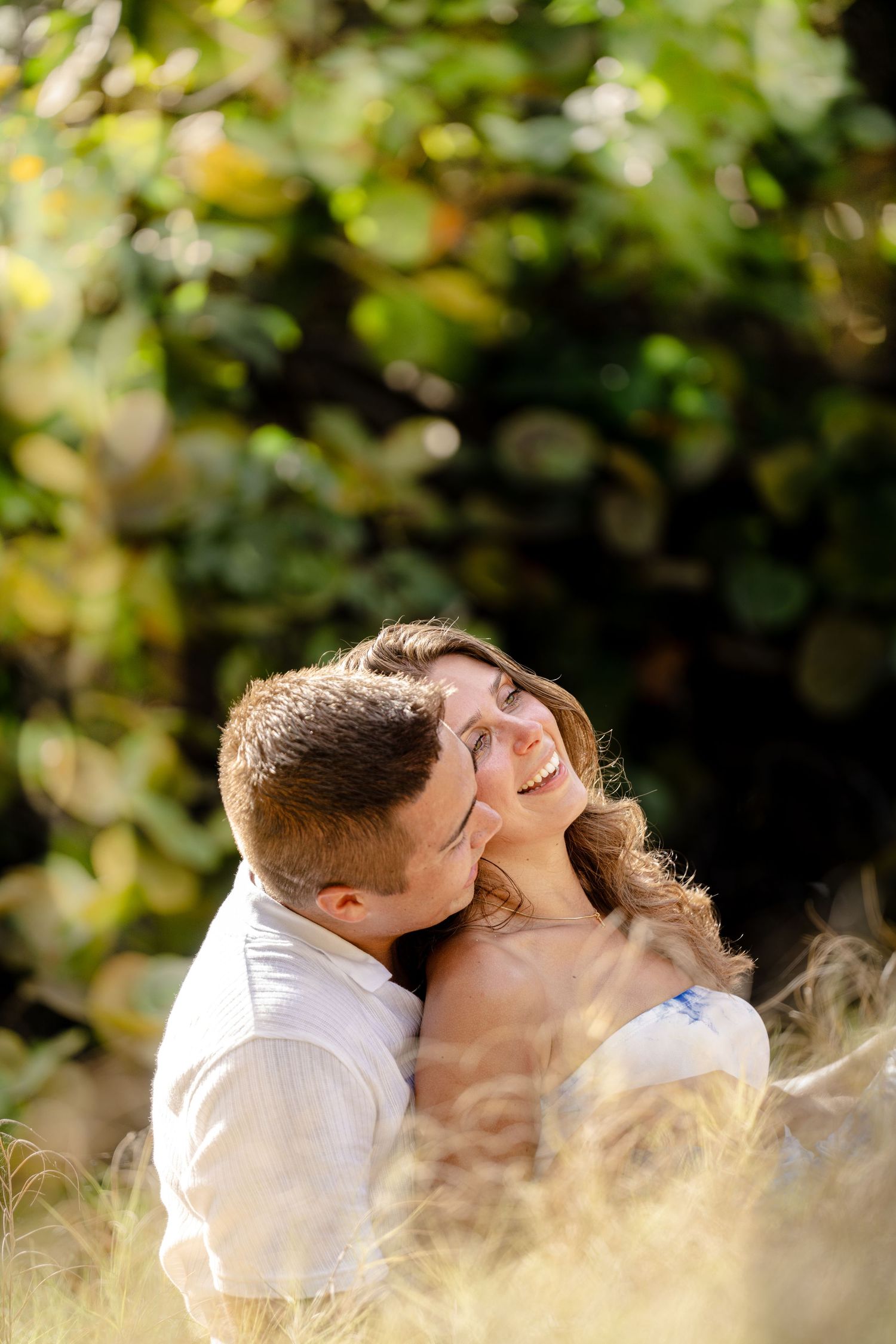 Romantic couple's portrait session among lush green foliage in natural lighting.