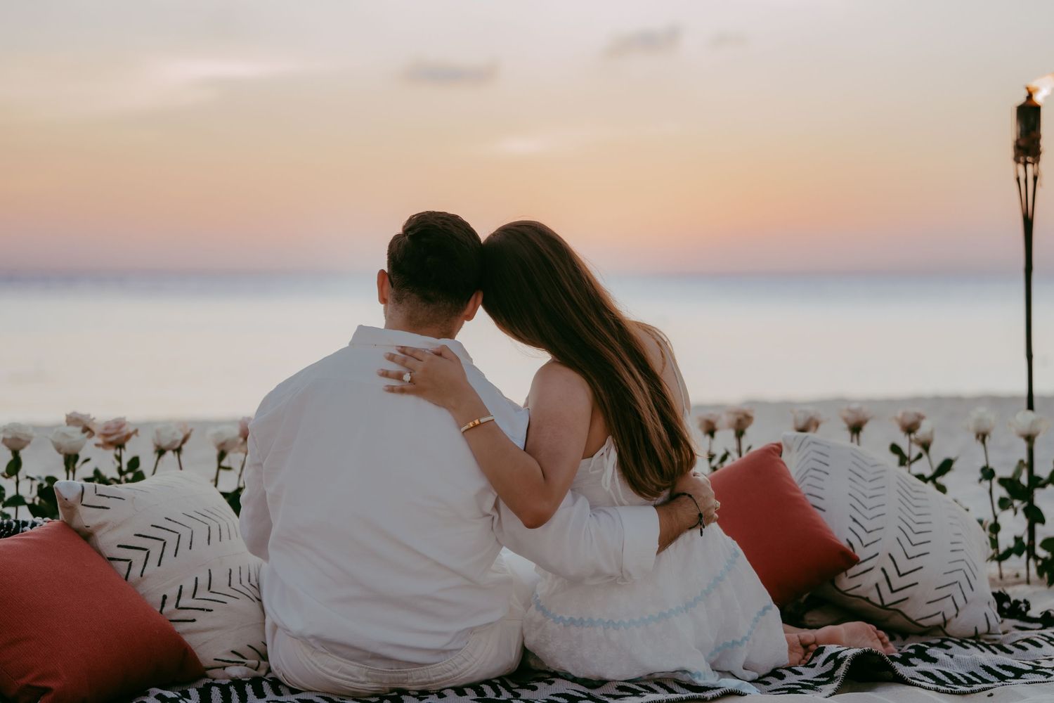Couple relaxing on striped blanket during golden hour at beach.